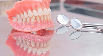Full set of dentures next to round dental mirrors on reflective tray